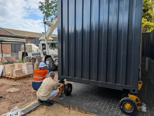 Container home rolled on skates through a tight side yard to its pad