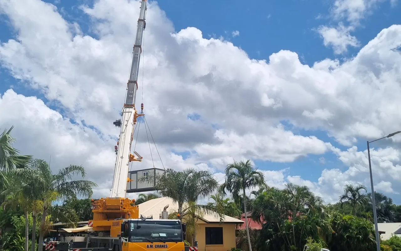 The unit suspended above a house roof, palms and the crane boom beside it
