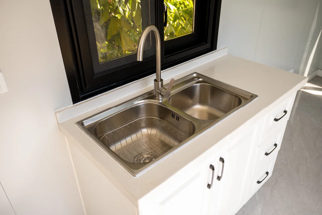A stainless double sink and white cabinets under a black-framed window
